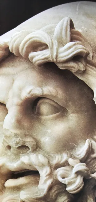 Close-up photograph of a marble head with curly hair and beard, eyes and open mouth in strong light and shadow — the face that inspired the logo.