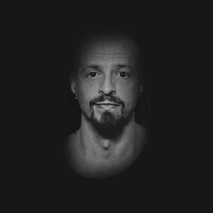 Black and white portrait of Alessio Maisano, bald with a goatee, looking straight at the camera.