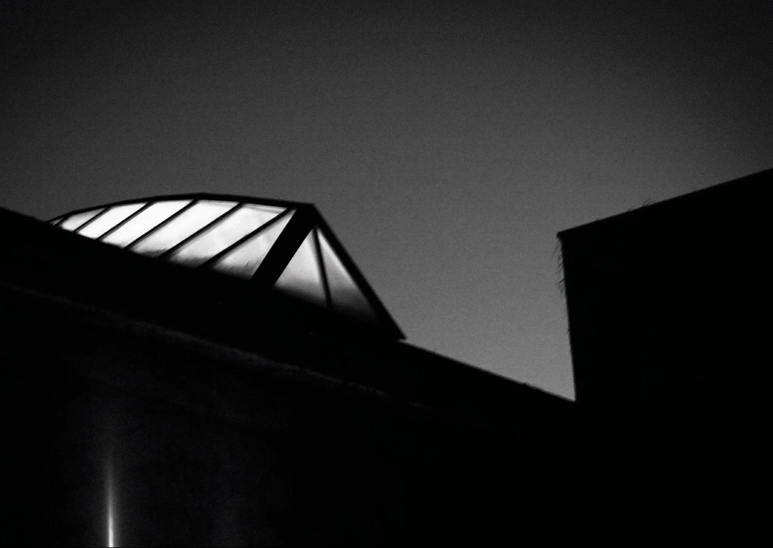 Black and white photograph of a glass skylight against a dark sky, seen from below.